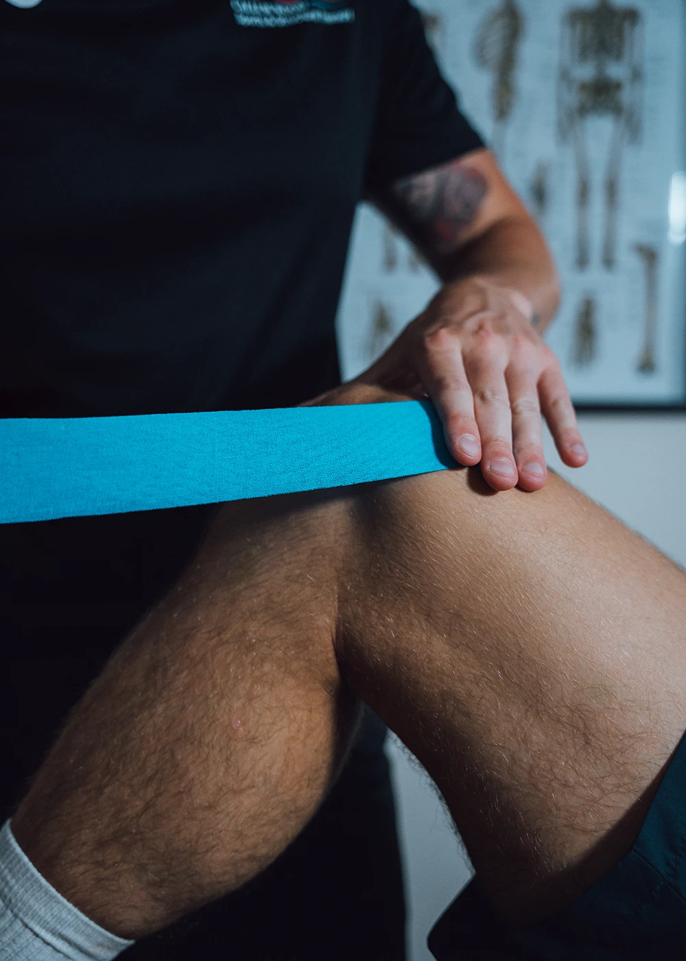 Callum applying blue sports kinesiology tape to a sportsman knee - Callum Wood Sports & Structural Therapy.